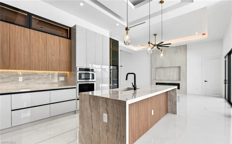 The kitchen features contemporary cabinetry, built-in appliances, and a central island with a natural stone countertop and sink