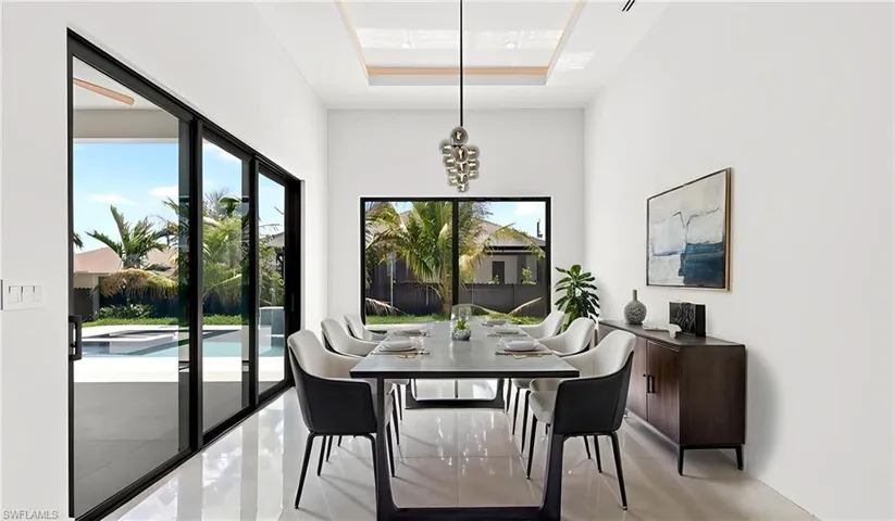 The dining area features white tile flooring, a contemporary chandelier, and large sliding glass doors providing outdoor views