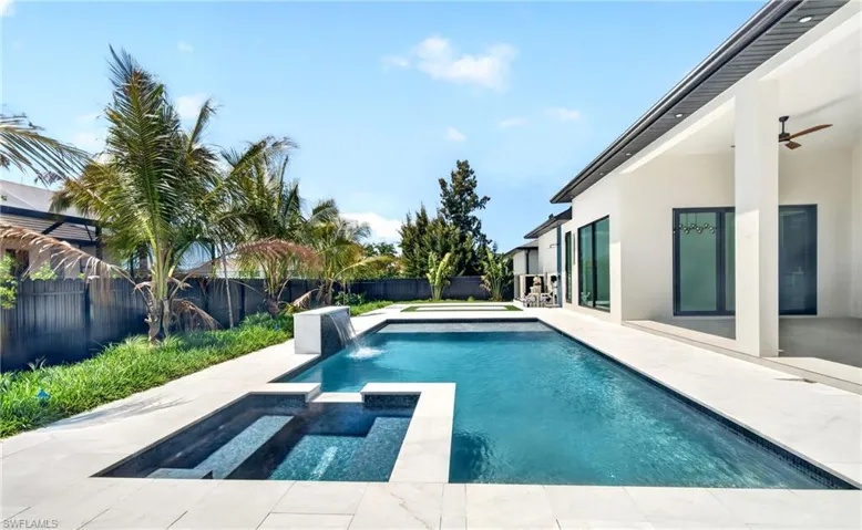 The property features a swimming pool with an integrated spa, surrounded by a paved patio and lush landscaping with palm trees
