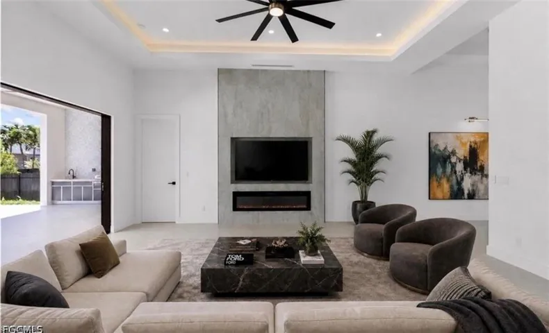 Expansive living area featuring a contemporary fireplace with a built-in television, tray ceiling with recessed lighting, and a modern ceiling fan