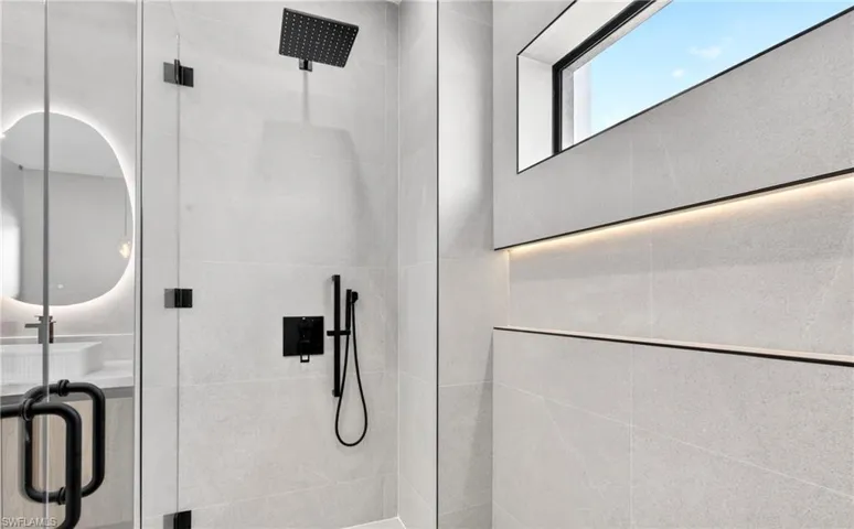 The shower features a matte black rain shower head and a handheld spray, set within a glass enclosure