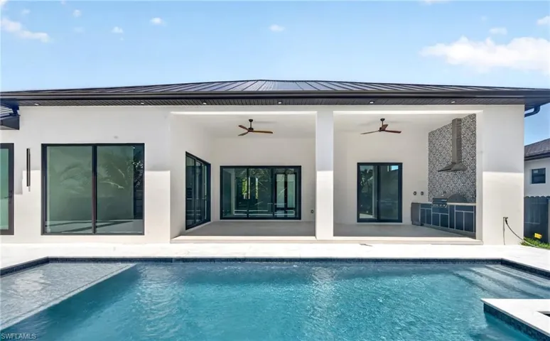 The property features an outdoor swimming pool, a covered patio area with ceiling fans, and an outdoor kitchen with a range hood and patterned backsplash