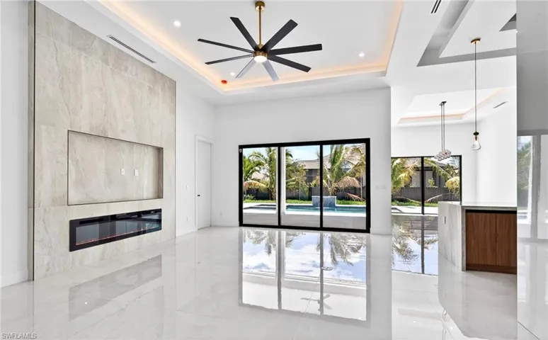 Spacious living area featuring light-colored tile flooring, a large decorative wall panel with an integrated fireplace and television niche, and a contemporary ceiling fan