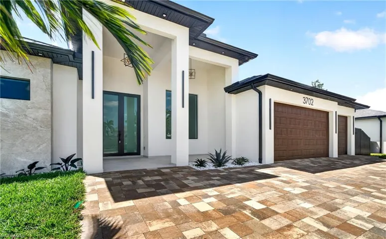 The property features a paver driveway, a two-car garage with brown doors, and a white exterior with dark accents
