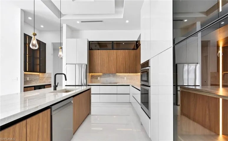 This modern kitchen features a large island with a sink and a built-in dishwasher, complemented by sleek white and wood cabinetry