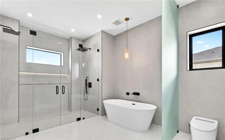 Modern bathroom featuring a freestanding tub, a spacious glass-enclosed shower with dual shower heads, and light gray tiled walls