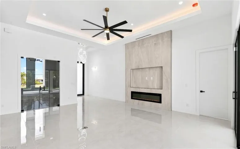 Spacious room featuring light-colored tile flooring, a tray ceiling with recessed lighting and a ceiling fan, and a fireplace with a textured stone facade