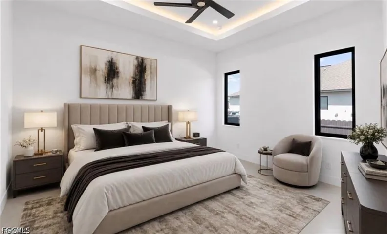 Recessed tray ceiling with integrated lighting, modern ceiling fan, two vertical windows with black frames, and light-toned flooring