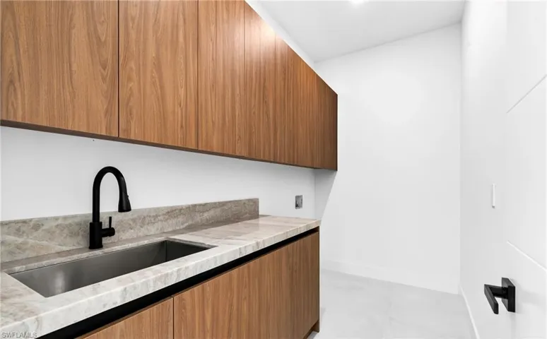 Utility area featuring wood cabinetry, a light-colored countertop, and a stainless steel sink with a black faucet