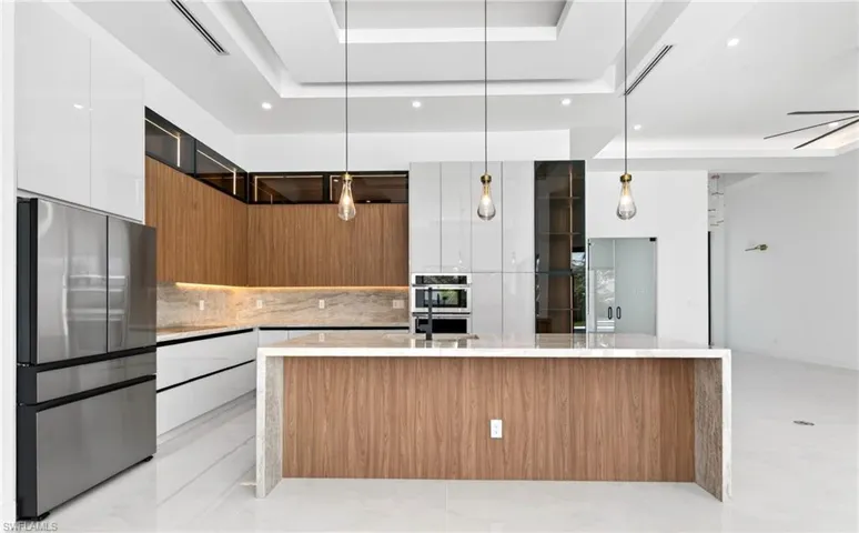 The kitchen features a large center island with a light-colored countertop, integrated stainless steel appliances, and a combination of white and wood-toned cabinetry