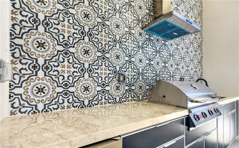 Outdoor kitchen area featuring patterned tile backsplash, a stainless steel range hood, and a built-in grill