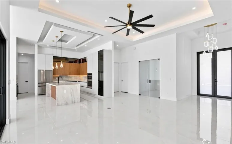 This open-concept living space features light-colored tile flooring, a modern kitchen with an island, and a distinctive ceiling fan