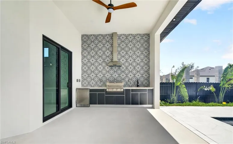 Outdoor living area featuring a built-in grill, patterned tile backsplash, and a ceiling fan