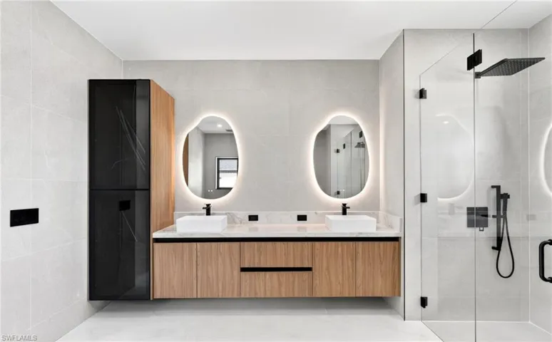 Contemporary bathroom featuring a floating vanity with dual vessel sinks, backlit mirrors, a glass-enclosed shower, and a tall storage cabinet with a dark glass front