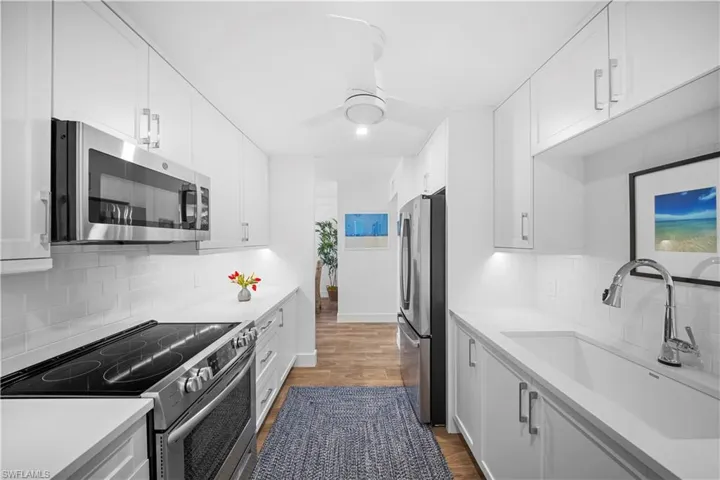 Kitchen with stainless steel appliances, white cabinetry, light wood finished floors, ceiling fan, and decorative backsplash