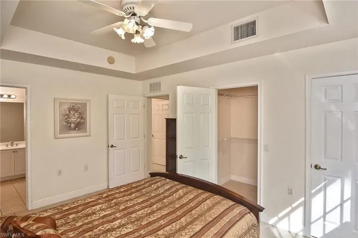Unfurnished bedroom with ensuite bath, ceiling fan, a spacious closet, a tray ceiling, and light tile patterned flooring