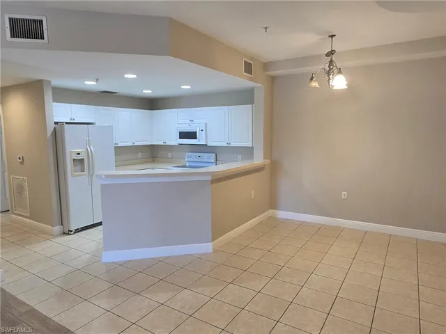 Kitchen with an inviting chandelier, white cabinetry, kitchen peninsula, white appliances, and pendant lighting