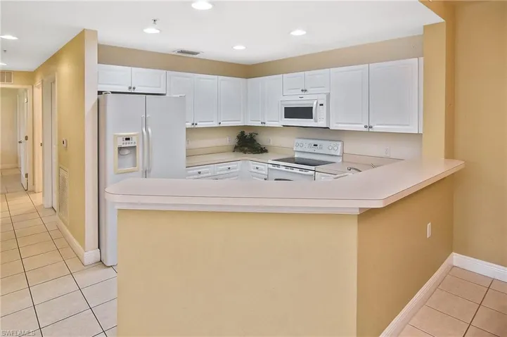 Kitchen with white cabinetry, light tile patterned flooring, white appliances, and kitchen peninsula