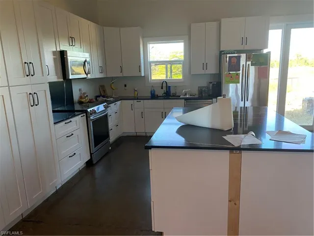 Kitchen featuring stainless steel appliances, white cabinetry, a kitchen island, and dark stone counters