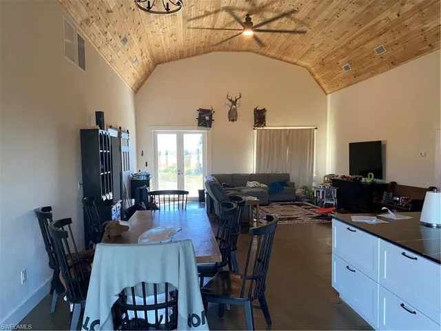 Dining space with wood ceiling, finished concrete flooring, high vaulted ceiling, ceiling fan, and french doors