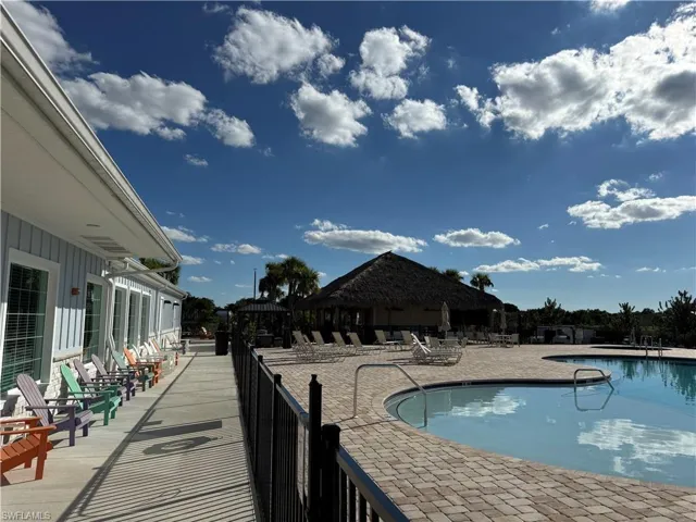 Swimming pool with paver decking, black metal perimeter fencing, and a thatch-roofed outdoor pavilion