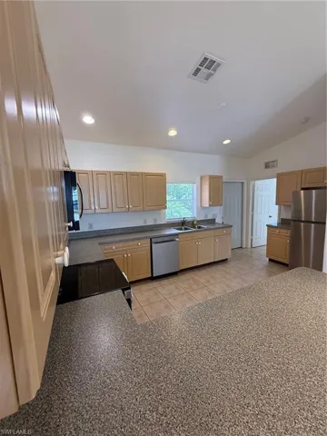 Kitchen featuring light wood-finish cabinetry, solid surface countertops, a stainless steel dishwasher, and a stainless steel refrigerator