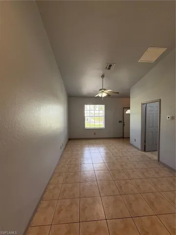 Spacious room featuring neutral-toned ceramic tile flooring, a window providing natural light, a ceiling fan with integrated lighting, and a neutral wall finish