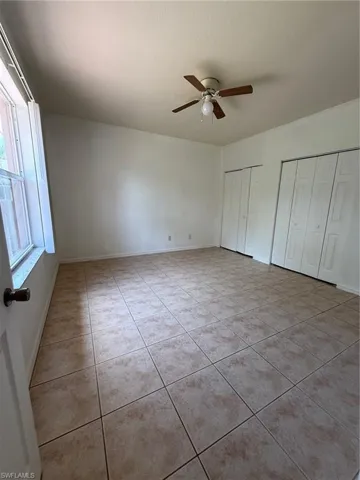 Spacious room featuring tile flooring, white walls, a ceiling fan with light fixture, and two sets of bi-fold closet doors