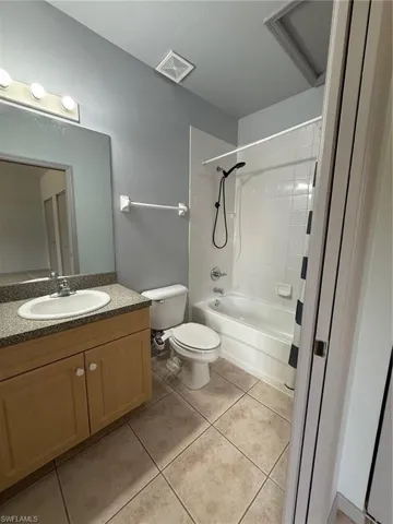 Full bathroom featuring a single vanity with wood-finish cabinetry and a stone-finish countertop, a tub-shower combination with white tile surround, and neutral-toned tile flooring