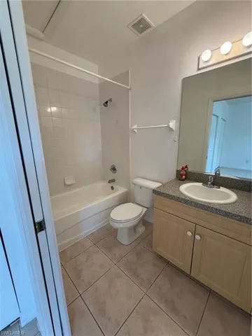Bathroom featuring a full-size tub with white tile surround, a single vanity with a speckled countertop, light wood-finish cabinetry, and a toilet