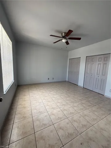 Spacious room featuring neutral wall tones, large format tile flooring, and a ceiling fan with integrated lighting
