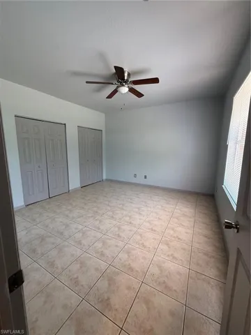 Spacious room featuring tile flooring, two bi-fold door closets, a ceiling fan with integrated lighting, and a window with blinds