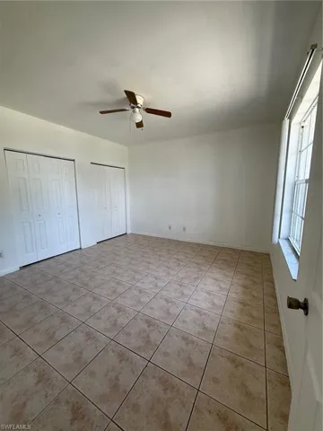 Spacious room featuring neutral-toned tile flooring, light-colored walls, and a ceiling fan with integrated lighting