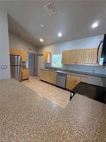 Kitchen featuring a breakfast bar with speckled countertops, stainless steel appliances, light wood-finish cabinetry, tile flooring, and recessed lighting