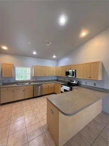 Kitchen featuring extensive light wood cabinetry, stone-finish countertops, stainless steel appliances, a breakfast bar, and tile flooring
