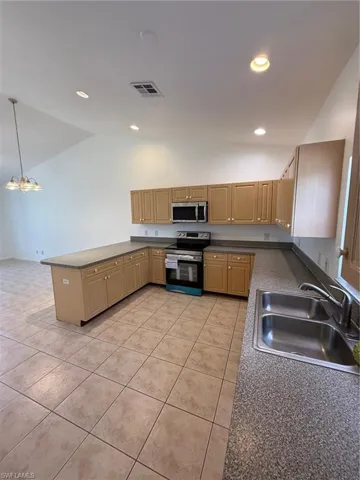 Kitchen featuring light wood cabinetry, stone-finish countertops, stainless steel appliances, and large format tile flooring