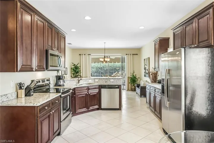 Kitchen with light stone countertops, stainless steel appliances, a notable chandelier, sink, and pendant lighting