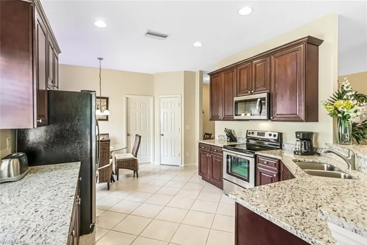 Kitchen with decorative light fixtures, light stone counters, stainless steel appliances, sink, and light tile patterned flooring
