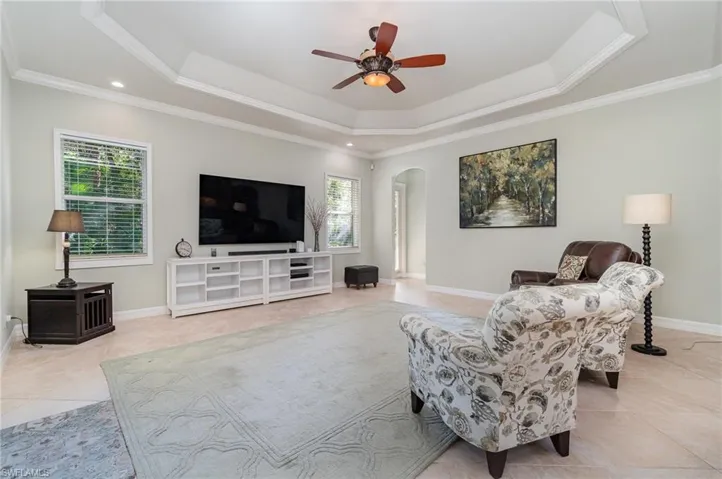 Family room with ceiling fan, a raised ceiling, ornamental molding, and light tile floors