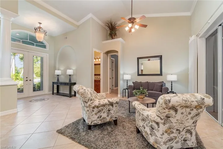 Tiled sitting room with french doors, decorative columns, ceiling fan, crown molding, and high vaulted ceiling