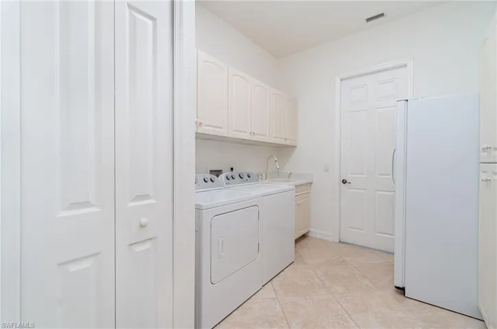 Laundry room with washing machine and clothes dryer, sink, light tile patterned flooring, and cabinets. Refrigerator and pantry cabinets to left
