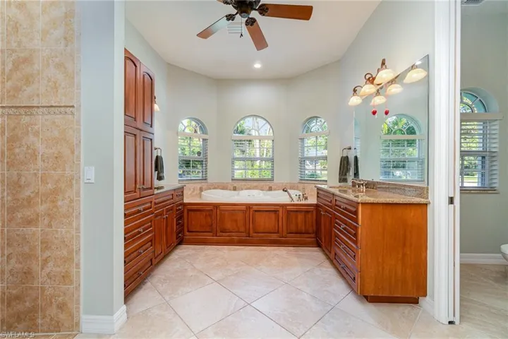 Primary Bathroom featuring tile flooring, ceiling fan, a tub to relax in, and double vanities