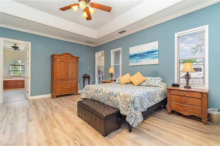 Bedroom with light vinyl flooring, ensuite bath, a tray  ceiling, ceiling fan, and crown molding