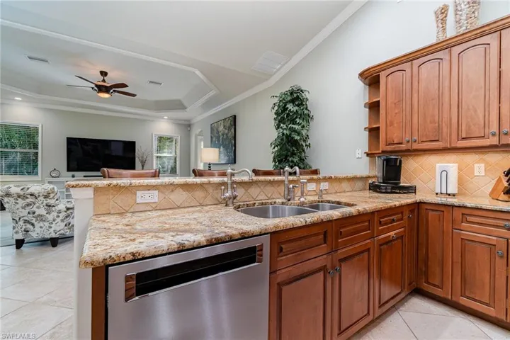 Kitchen with dishwasher, crown molding, sink, light stone countertops, and kitchen peninsula