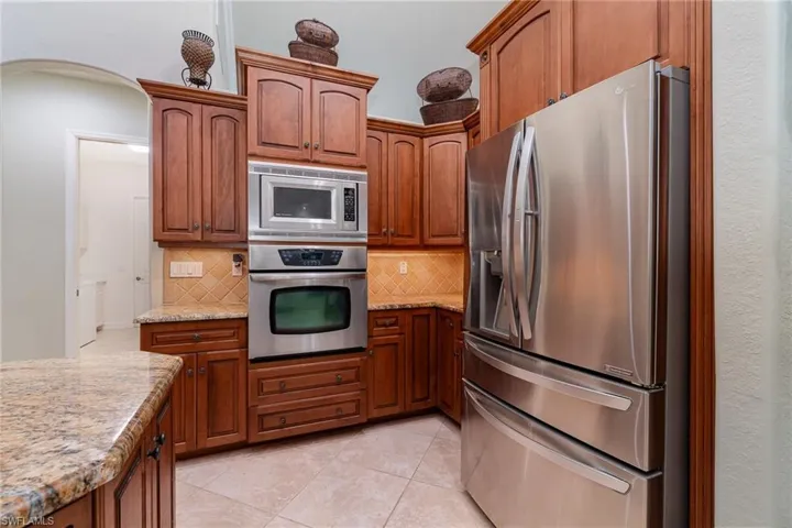 Kitchen featuring backsplash, light stone countertops, light tile patterned floors, and stainless steel appliances