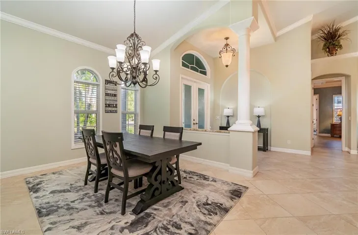 Tiled dining room with a high ceiling, an inviting chandelier, french doors, ornate columns, and ornamental crown molding