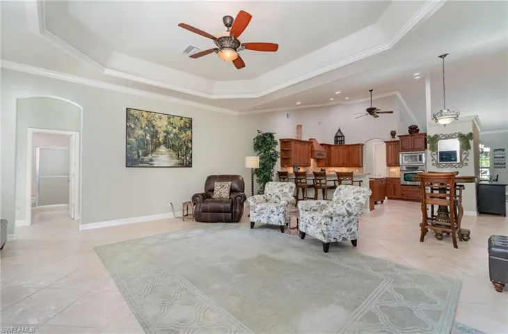 Family room featuring ceiling fan, a tray ceiling, ornamental molding, and light tile  floors