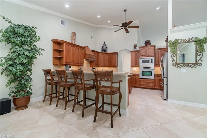 Kitchen featuring crown molding, decorative backsplash, a towering ceiling, appliances with stainless steel finishes, and a kitchen bar