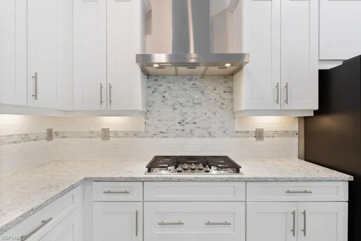 Kitchen with wall chimney exhaust hood, freestanding refrigerator, stainless steel gas cooktop, and white cabinets