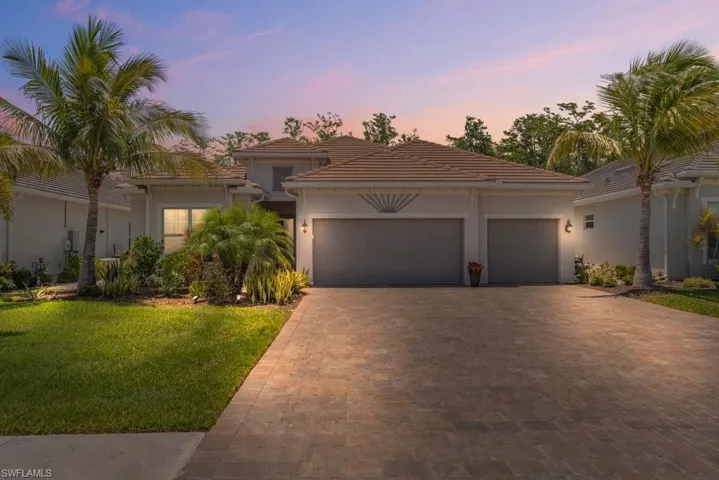 View of front of property with decorative driveway, an attached garage, a lawn, stucco siding, and a tile roof